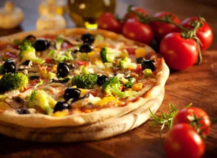 A vegetable pizza with broccoli, olives and peppers beside fresh tomatoes