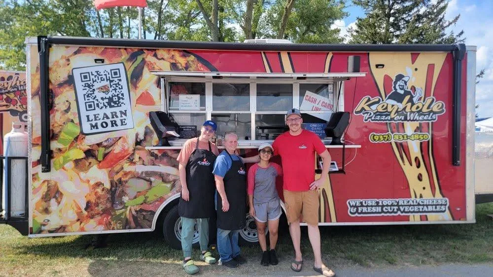 Four members of the Keyhole Pizza On Wheels crew standing in front of the red trailer
